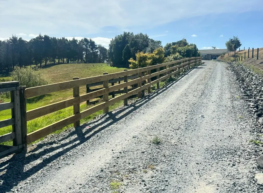 Completed post and rail fence lining a gravel farm driveway